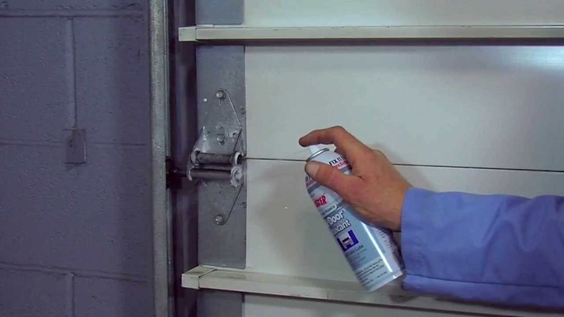 A man spraying garage door lubricant on the hinges