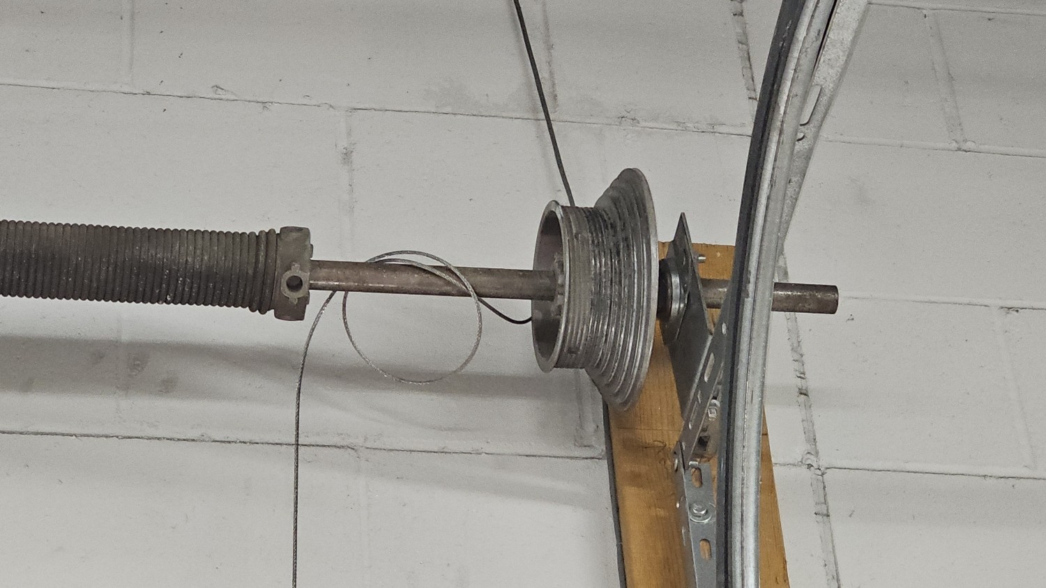 Commercial garage door repair showing a torsion spring, cable drum, and loose lift cable on an industrial overhead door.