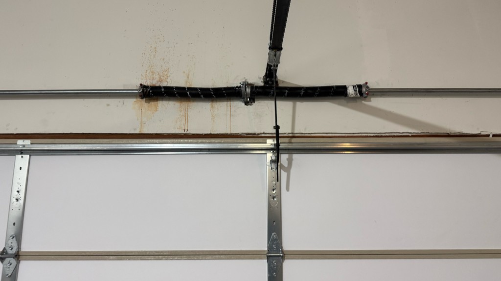 Garage door maintenance services showing a torsion spring, opener arm, and track hardware inspected above a residential garage door.