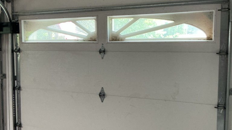Garage door maintenance showing a residential sectional door with decorative windows, hinges, and track hardware.